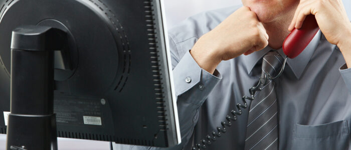 Focused businessman listening to telephone on landline phone looking at screen sitting in office.