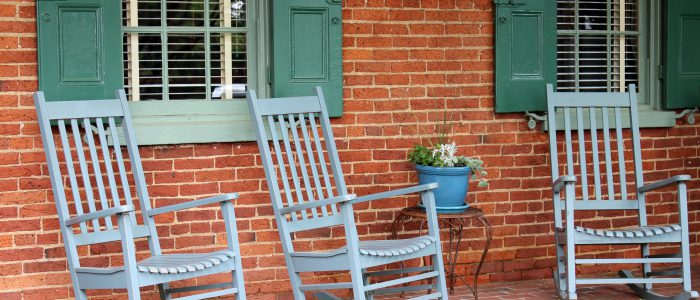 Rocking Chairs in front of a house with brick walls and green shutters.