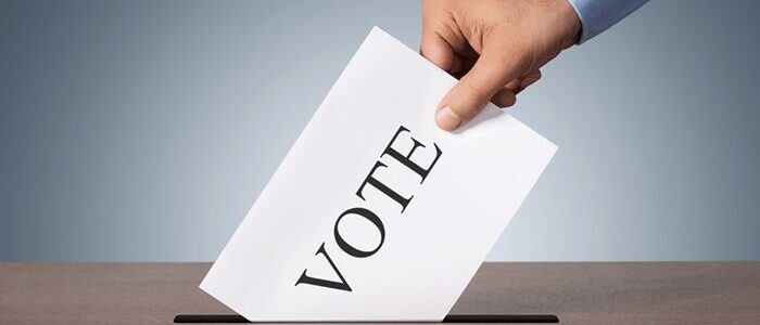 Hand dropping ballot labeled VOTE into slot