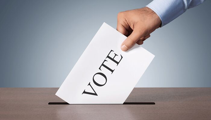 Hand dropping ballot labeled VOTE into slot