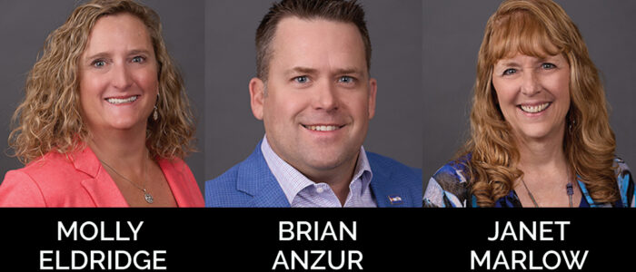 Three smiling people against a gray background.